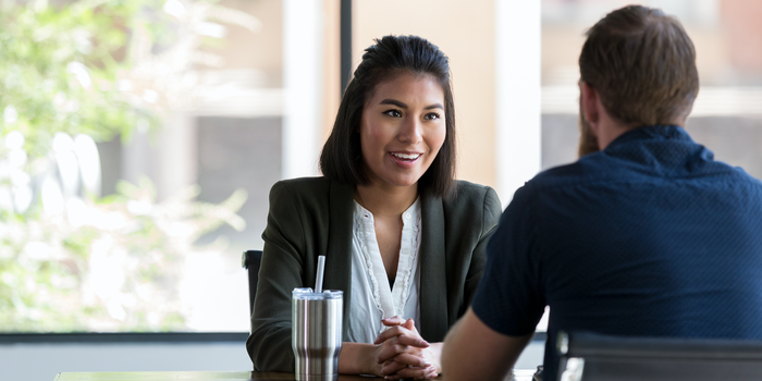 two people sitting across a table from one another (only one person's face visible) during a job interview