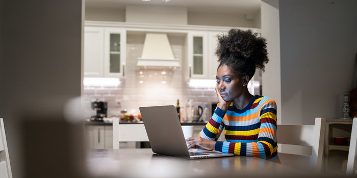 unhappy person sitting at dining room table working on laptop