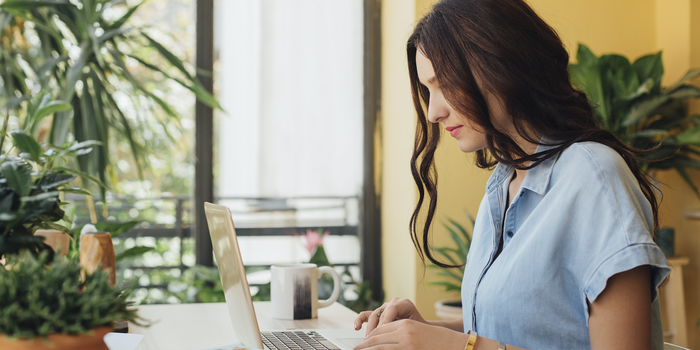 person sitting at a table typing on laptop with a coffee mug and plants nearby