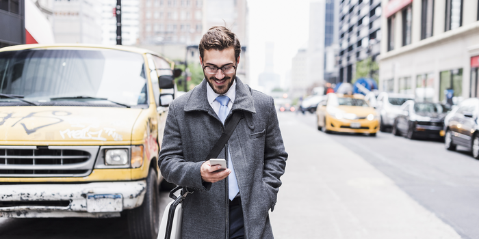 person walking down the street in business attire looking at their phone and smiling