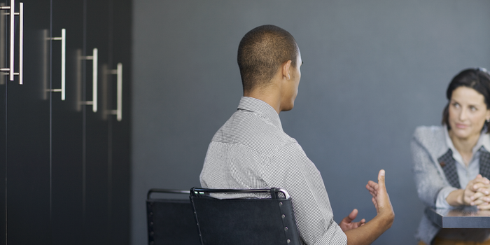 two people sitting in a conference room at a job interview, one of them speaking and gesturing with their hands