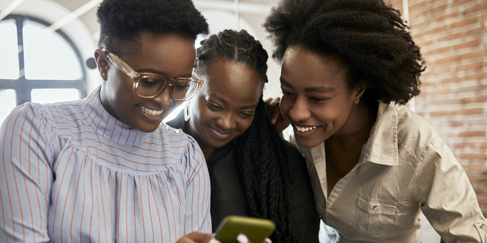 three coworkers looking at a smartphone screen and laughing