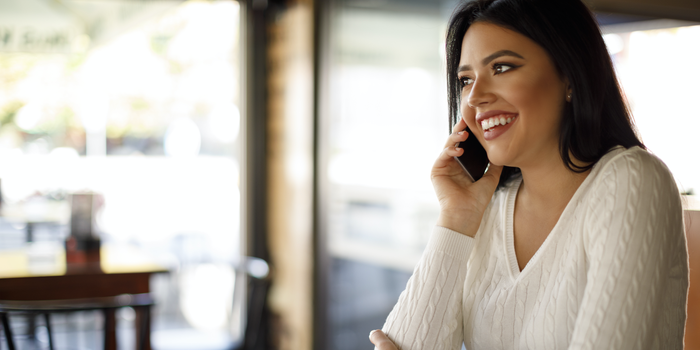 person sitting at a cafe speaking on a cell phone and smiling