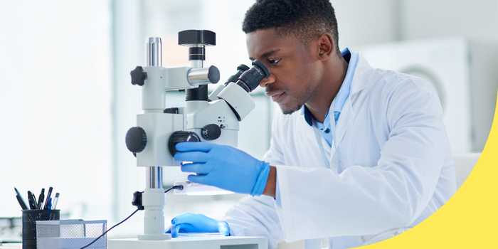 person sitting down in a lab and looking through a microscope