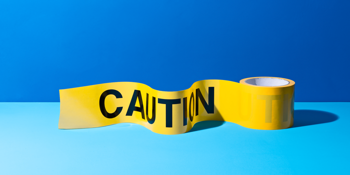 roll of yellow caution tape with black lettering unspooling just enough to see one “Caution” set against a two-toned blue background