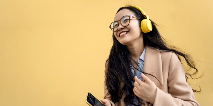 person holding their cell phone, wearing over-ear headphones, and smiling against a yellow background