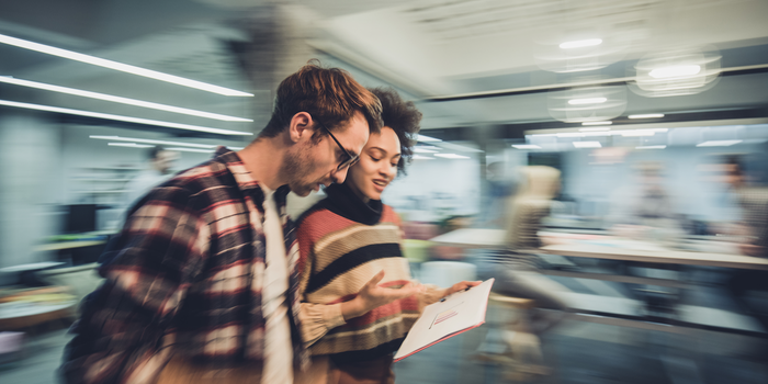 two people standing in an office looking at a report with blurred motion all around them