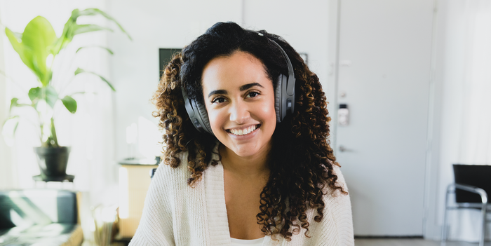 remote worker sitting at home wearing headphones and smiling, a plant, couch, and TV visible in the background