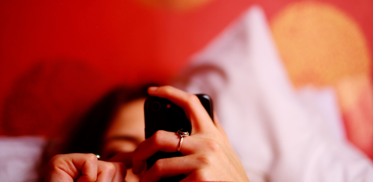 person looking at smartphone while lying on bed