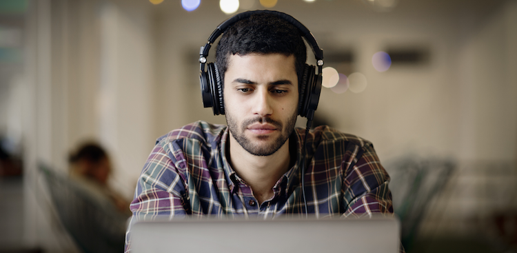 person wearing headphones and looking at laptop screen/Getty Images