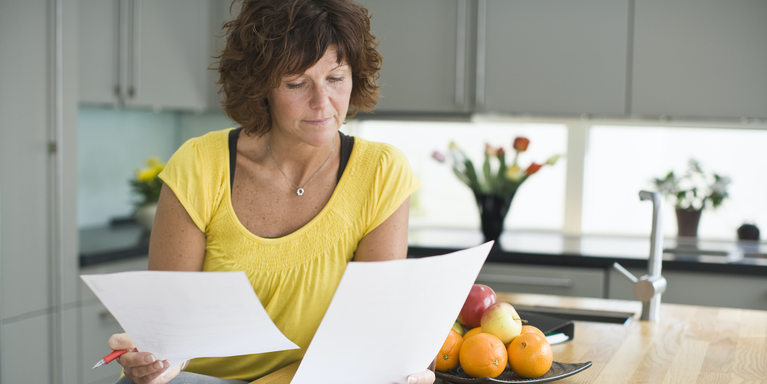 person sitting in their kitchen holding and looking at two sheets of paper