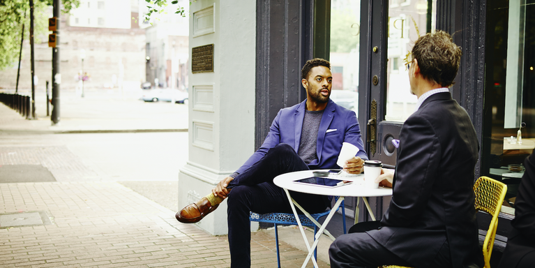 two people sitting at a table outside of a coffee shop for a professional meeting