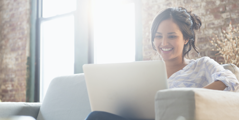 person sitting on couch, looking at laptop and smiling