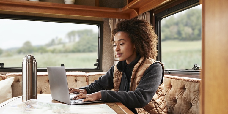person sitting in a camper van in a puffy vest and typing on a laptop